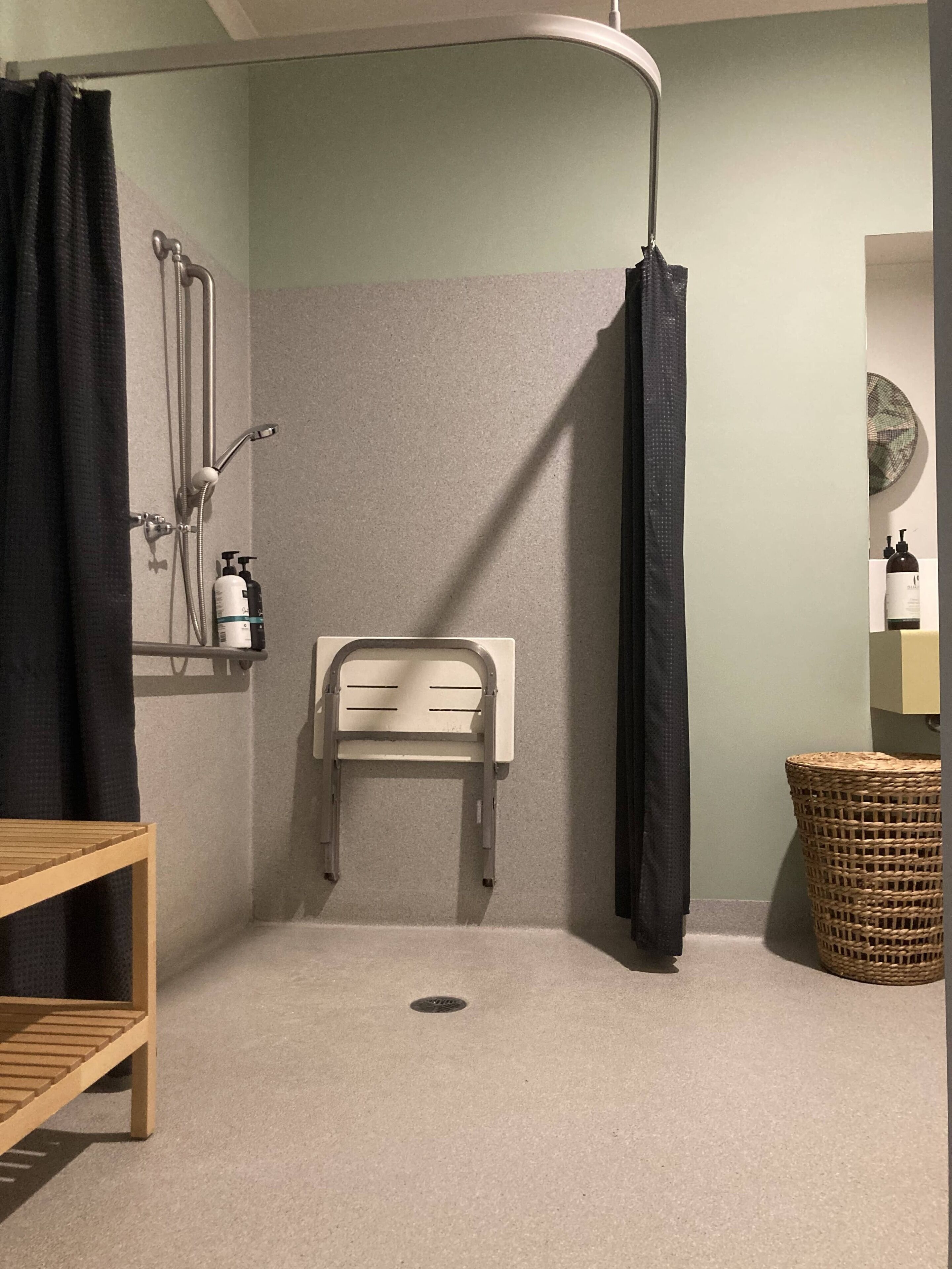 A shower area with a showerhead, a towel rack, and a small wooden shelf.