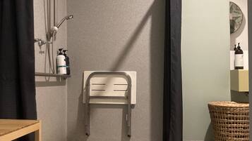 A shower area with a showerhead, a towel rack, and a small wooden shelf.