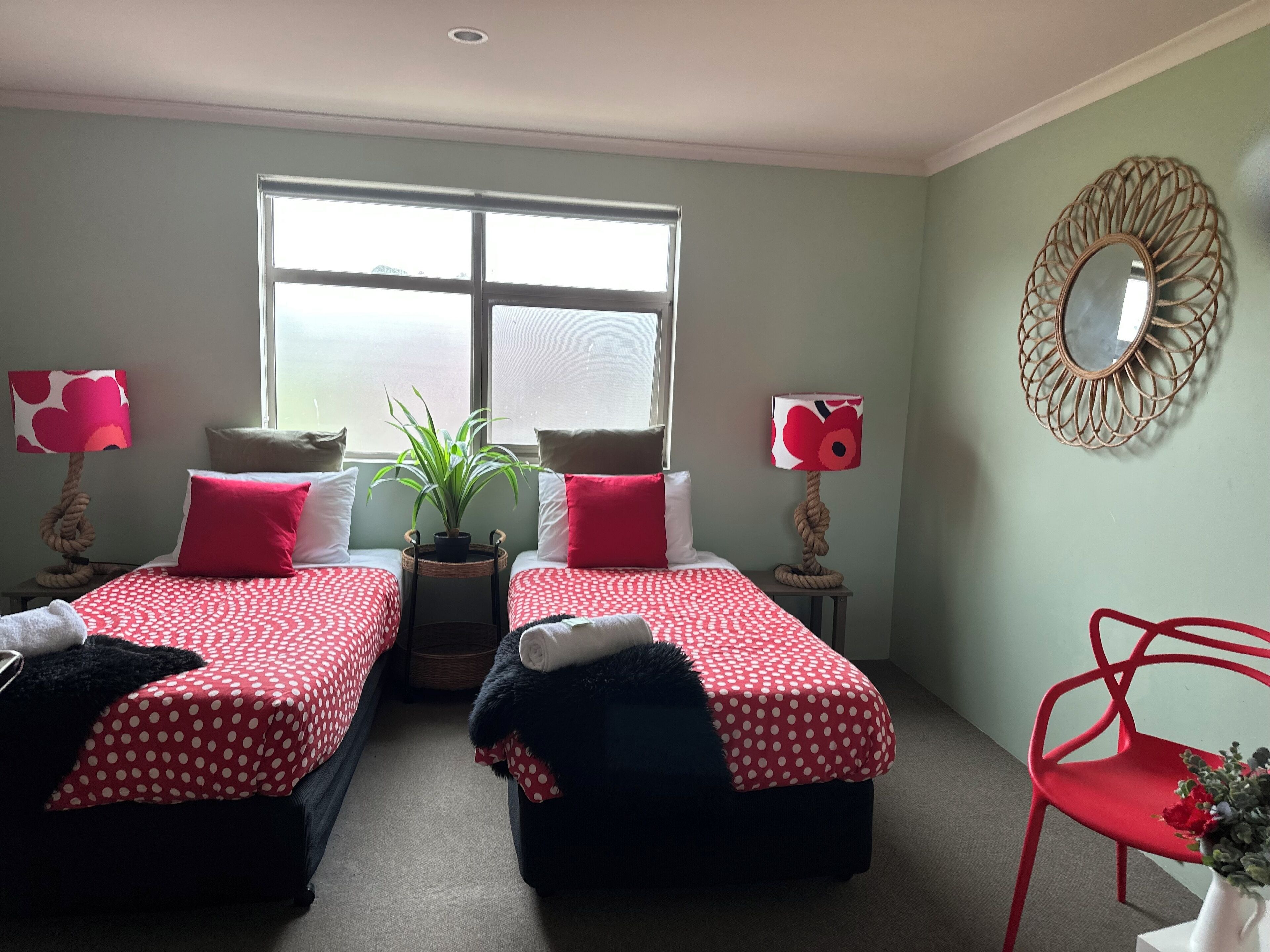 Una habitación con dos camas, cada una con un edredón rojo de lunares, una planta en maceta y un espejo en la pared.