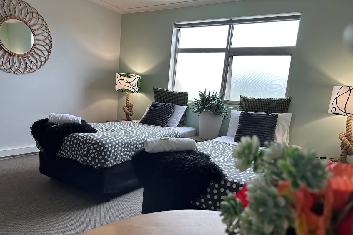 A bedroom with two beds, a potted plant, and a window with blinds.