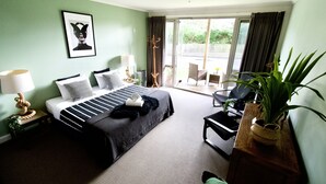 Une chambre d’hôtel avec un lit, une chaise, une table, une lampe, une plante et une vue sur l’extérieur.