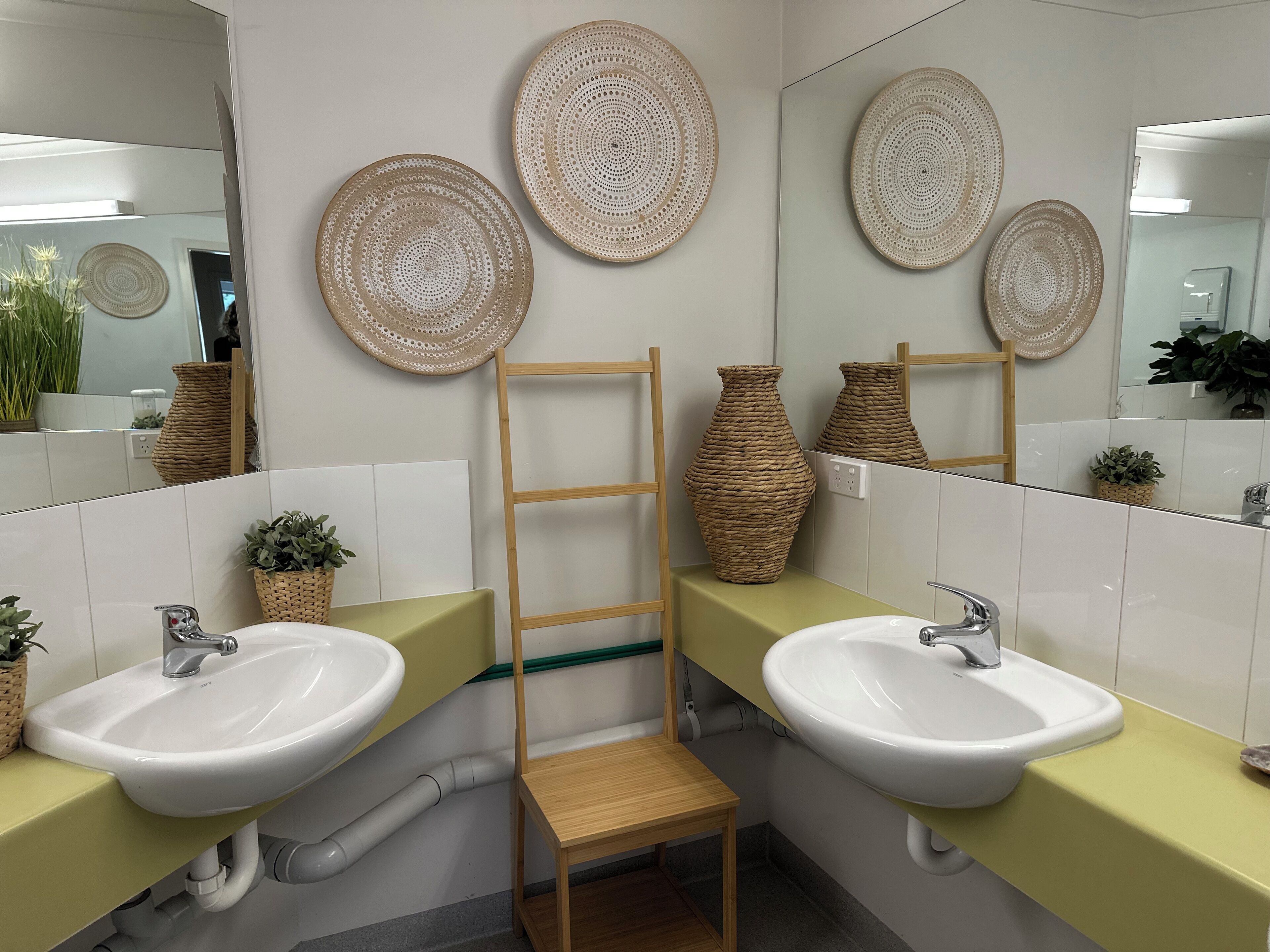 Un baño con dos lavamanos, una escalera de madera y adornos tejidos en la pared.