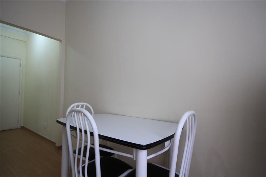A small, white table with four chairs in a room with plain walls and a door.