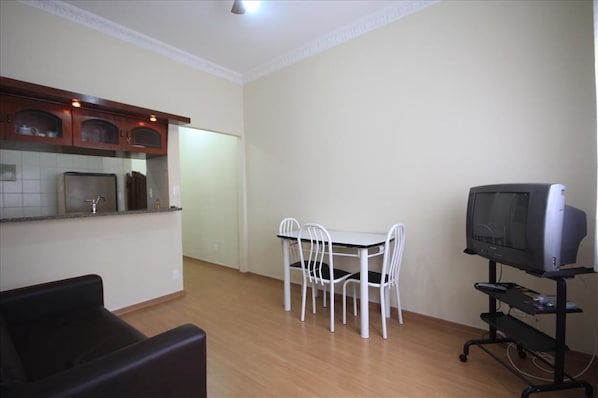 A compact living space with a kitchenette, a dining area with a table and chairs, and a television on a stand.