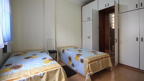 Quarto com duas camas de solteiro, uma cadeira e um guarda-roupa.