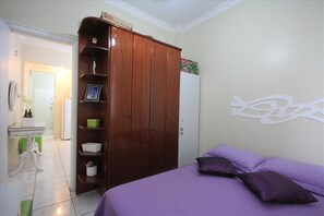 Un dormitorio con cama, ropa de cama púrpura, un armario y un adorno en la pared.