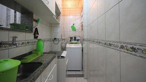 A narrow kitchen with white tiles, a built-in oven, and a sink with green dish racks. - Dutra 1104 (Rio de Janeiro)