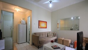 A living room with a sofa, coffee table, and a television. There is a refrigerator and a microwave in the kitchen area. - Dutra 1104 (Rio de Janeiro)