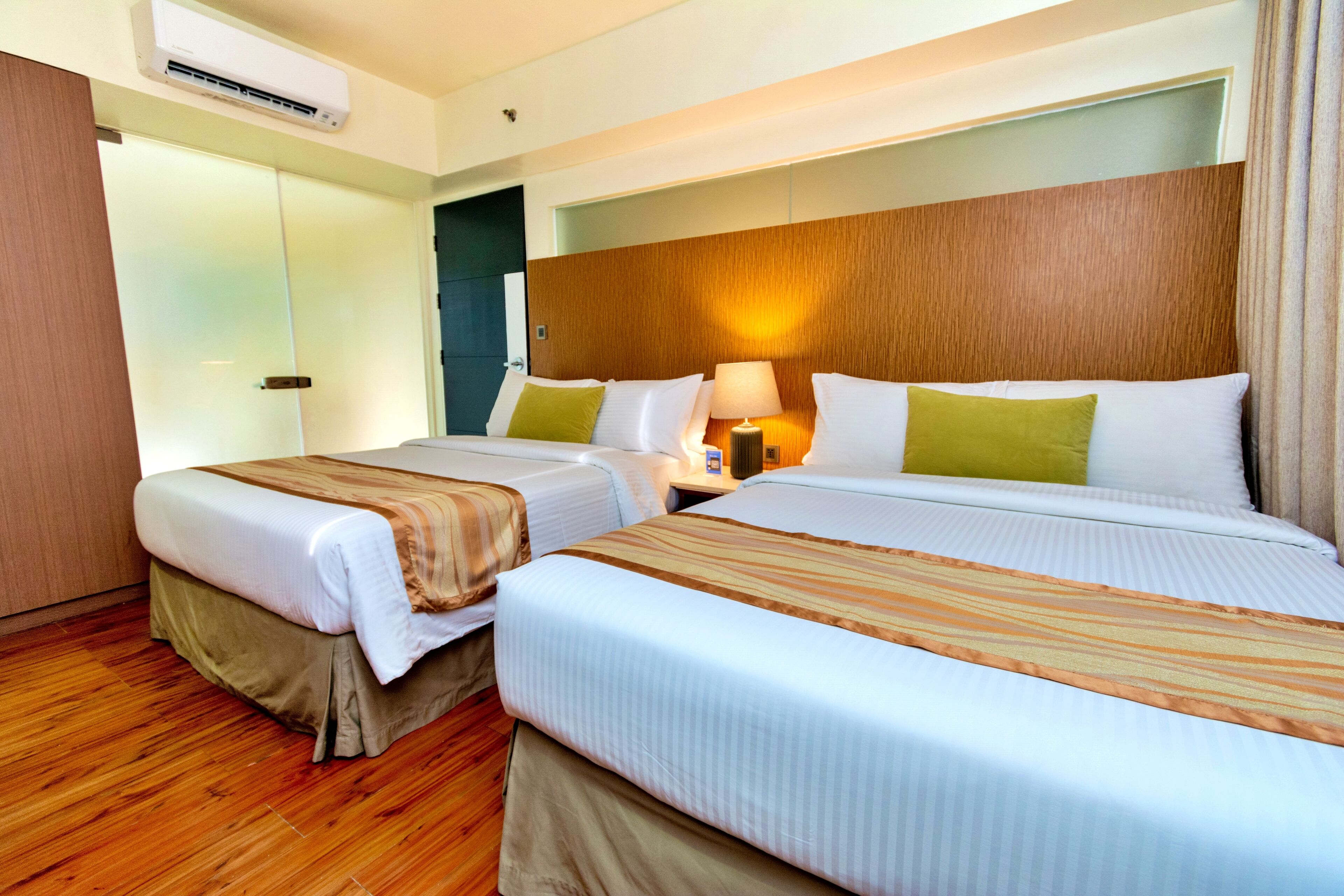 A hotel room with two beds, a wooden headboard, a nightstand with a lamp, and a sliding door closet.