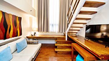 Una sala de estar moderna con una escalera de madera, un sofá con cojines azules y un televisor de pantalla plana sobre una mesa de madera.