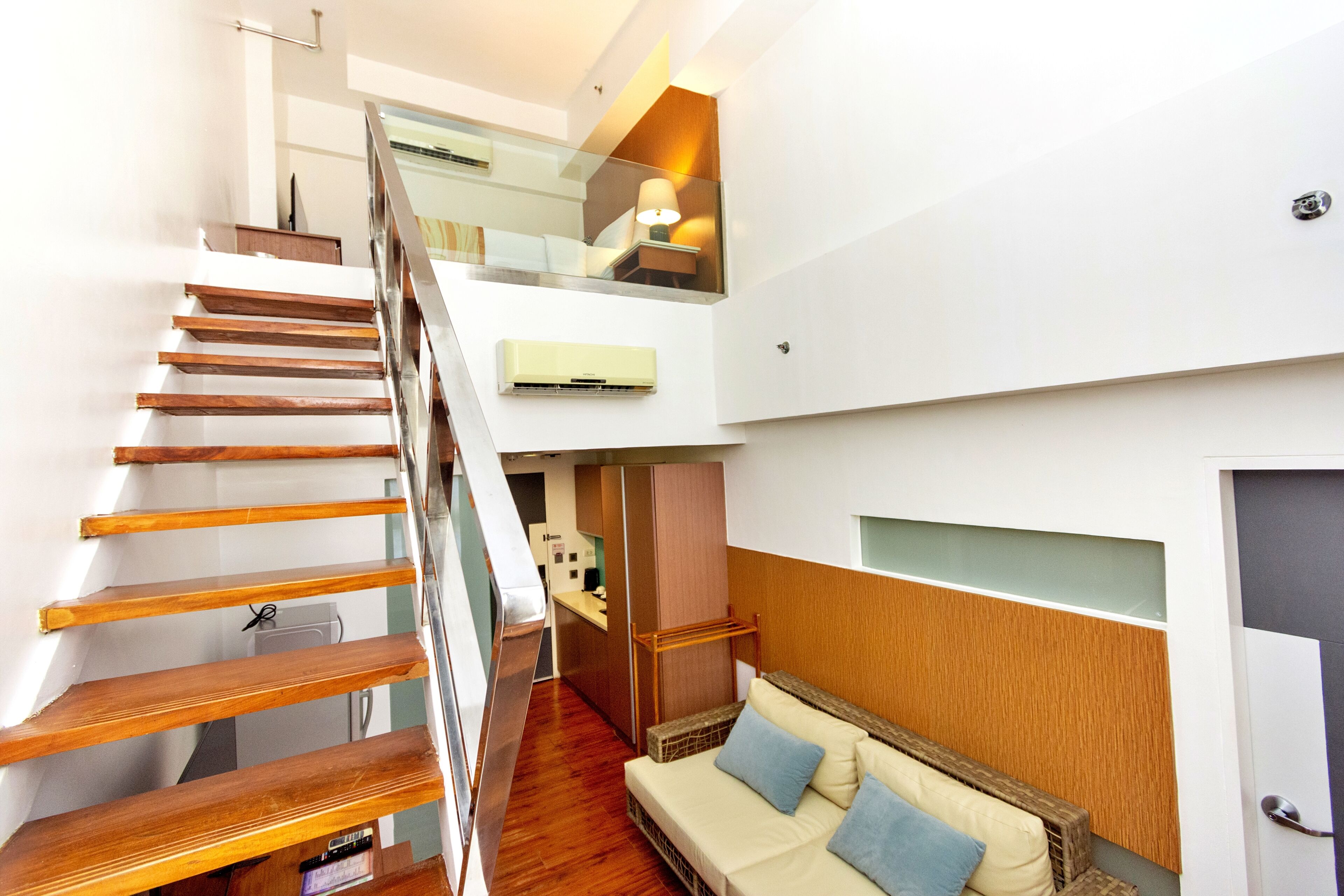 Un intérieur moderne avec un escalier en bois, un canapé agrémenté de coussins et un coin cuisine.