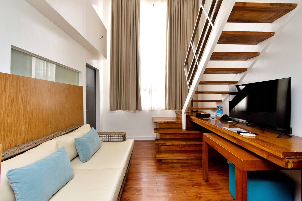 A modern living room with a sofa, wooden staircase, and a television.