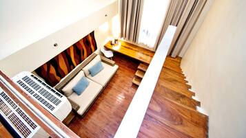 Una habitación de hotel moderna con suelo de madera, un sofá con cojines azules, una mesita con lámpara y una escalera.