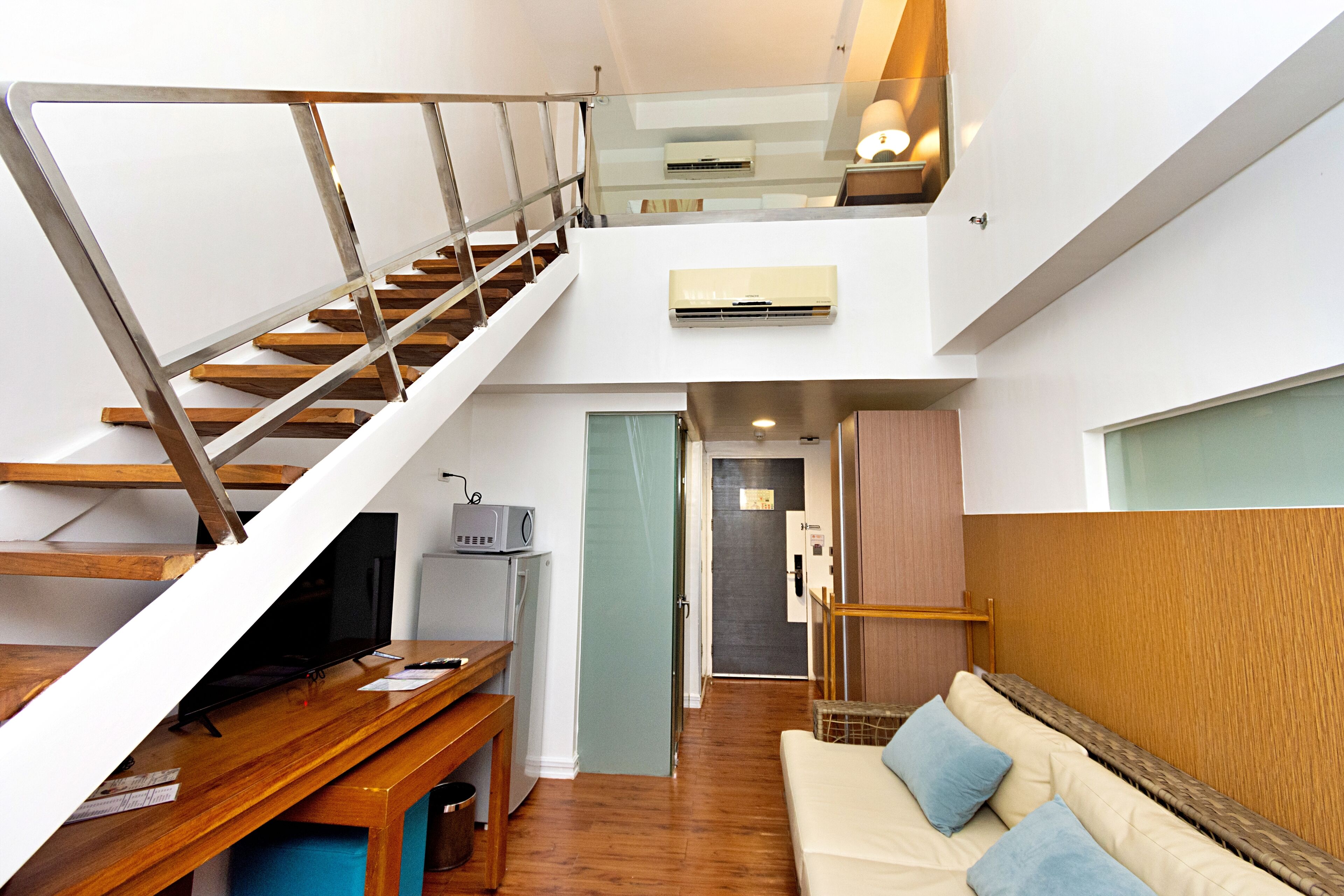 A modern apartment with a staircase, a living area, a kitchenette, and a separate bedroom.
