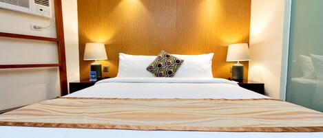 Una habitación de hotel con una cama grande, dos lámparas de noche, un cabecero de madera y un aire acondicionado instalado en la pared.
