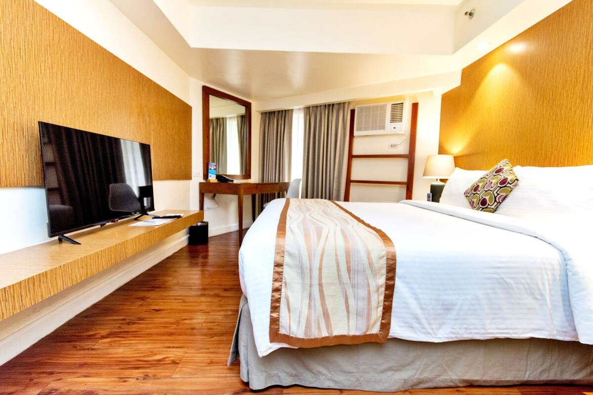 A hotel room with a bed, a TV, a desk, and a mirror.