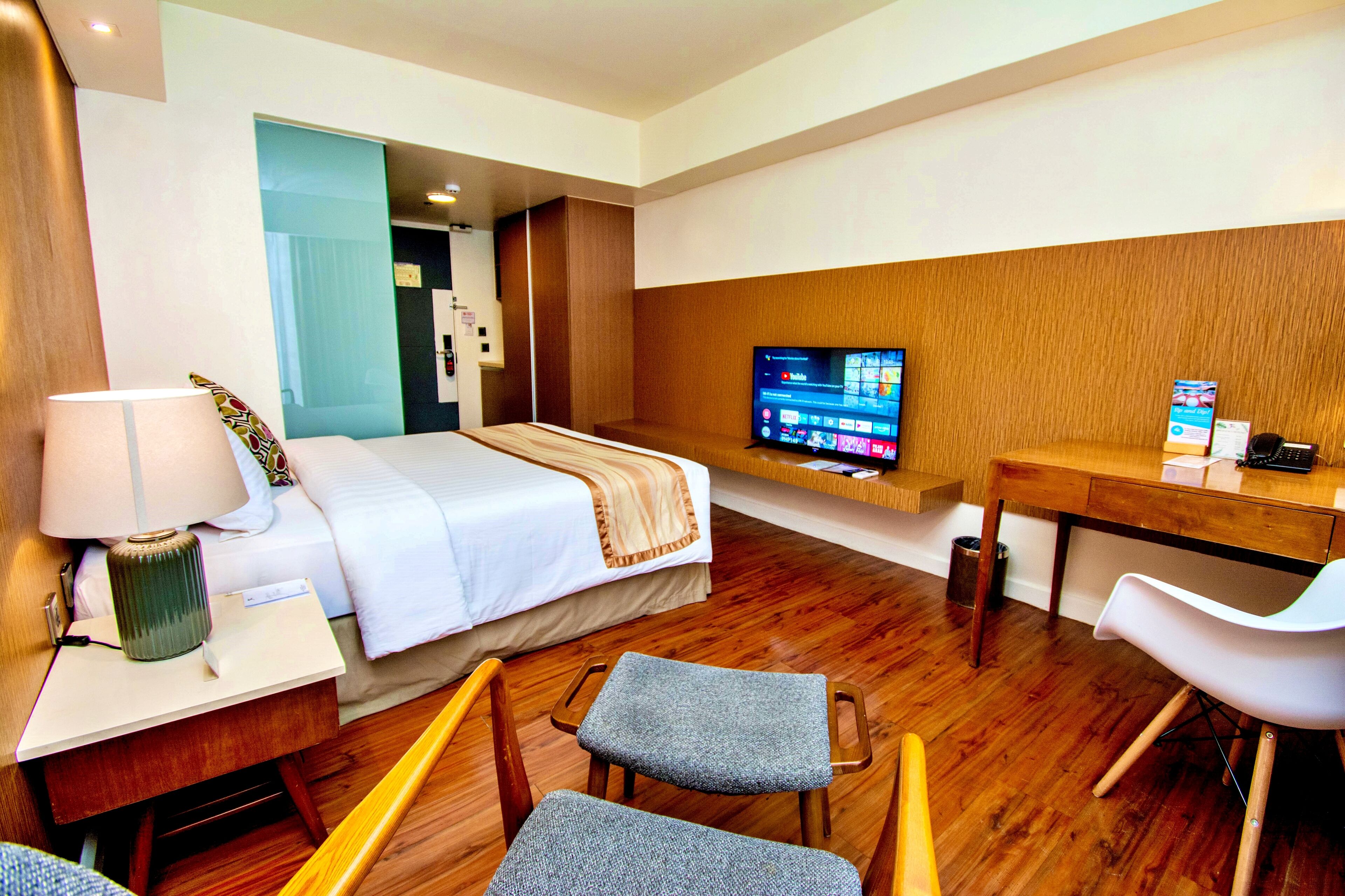 Ein Hotelzimmer mit Bett, Schreibtisch mit Lampe, Fernseher auf einem Standfuß und einem Sessel.