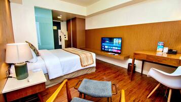 Ein Hotelzimmer mit Bett, Schreibtisch mit Lampe, Fernseher auf einem Standfuß und einem Sessel.