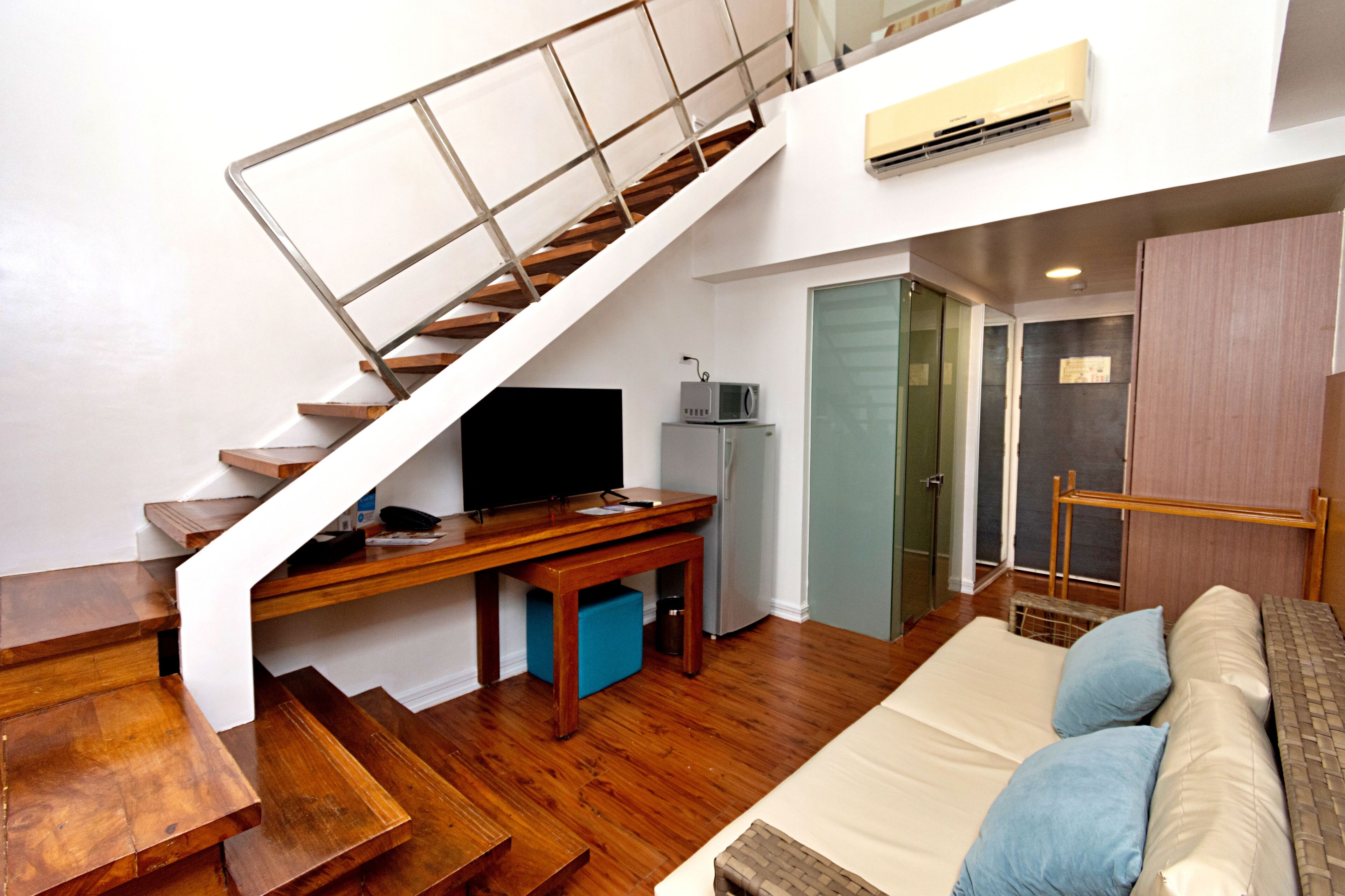 Een moderne woonruimte met een houten trap, een flatscreen televisie, een klein tafeltje, een bank en een deur naar een andere kamer.
