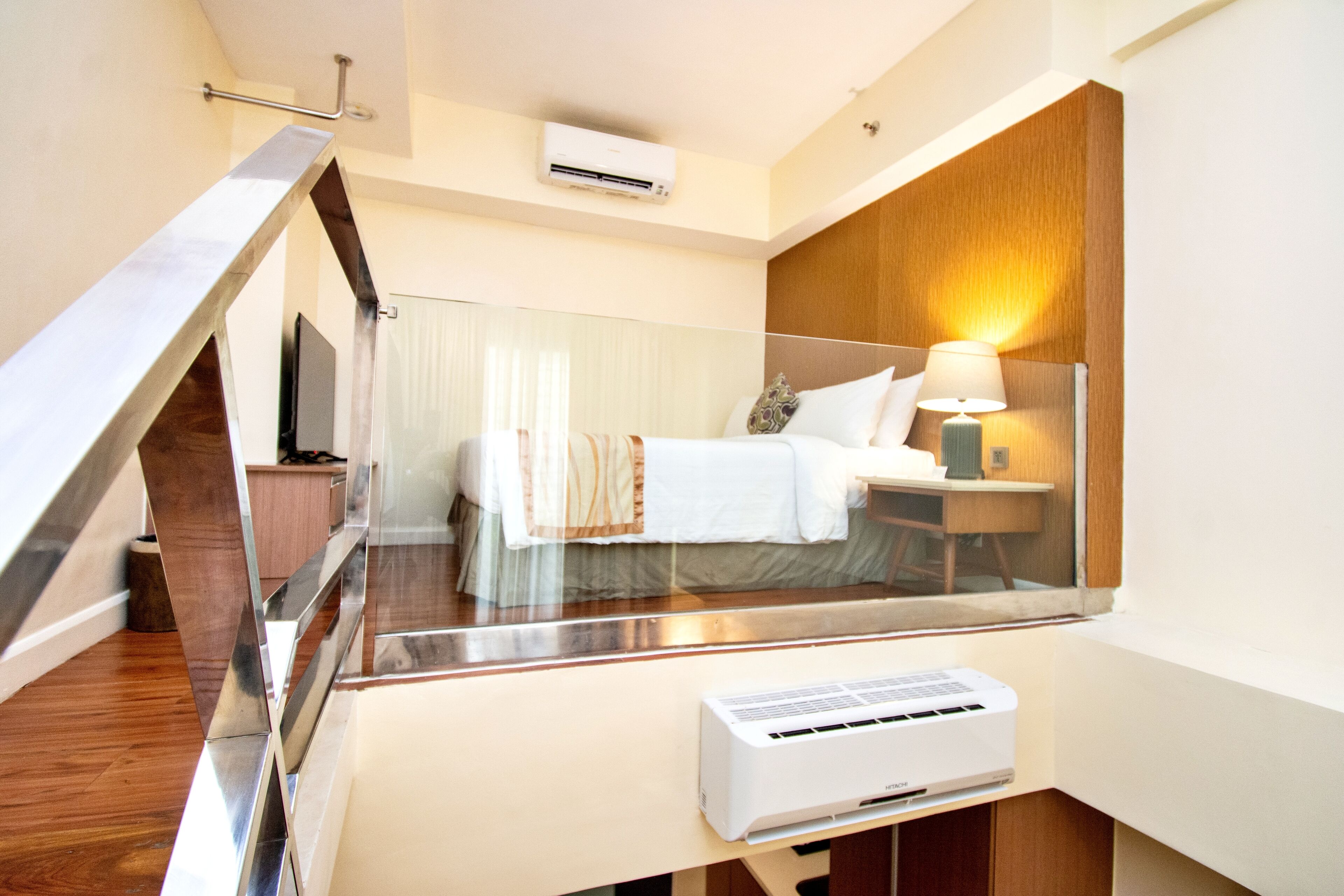 A modern hotel room with a bed, bedside table, lamp, air conditioning unit, and a view through a glass partition.