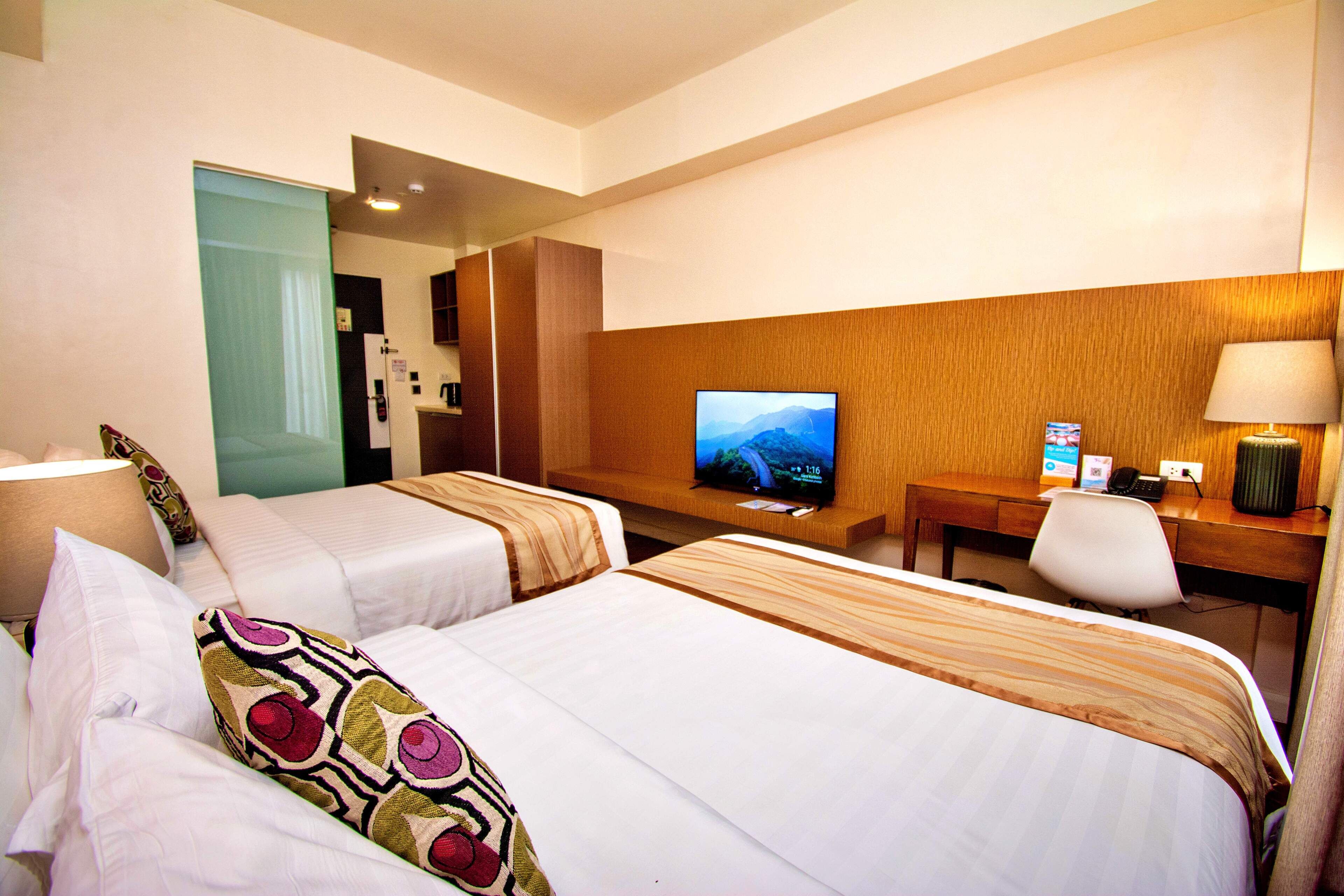 Une chambre d’hôtel avec deux lits, un bureau avec une télévision, une chaise et une lampe.