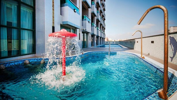 A swimming pool with a water fountain, a tiled deck, and a modern building with balconies. - Yaling Hotel (Magong)