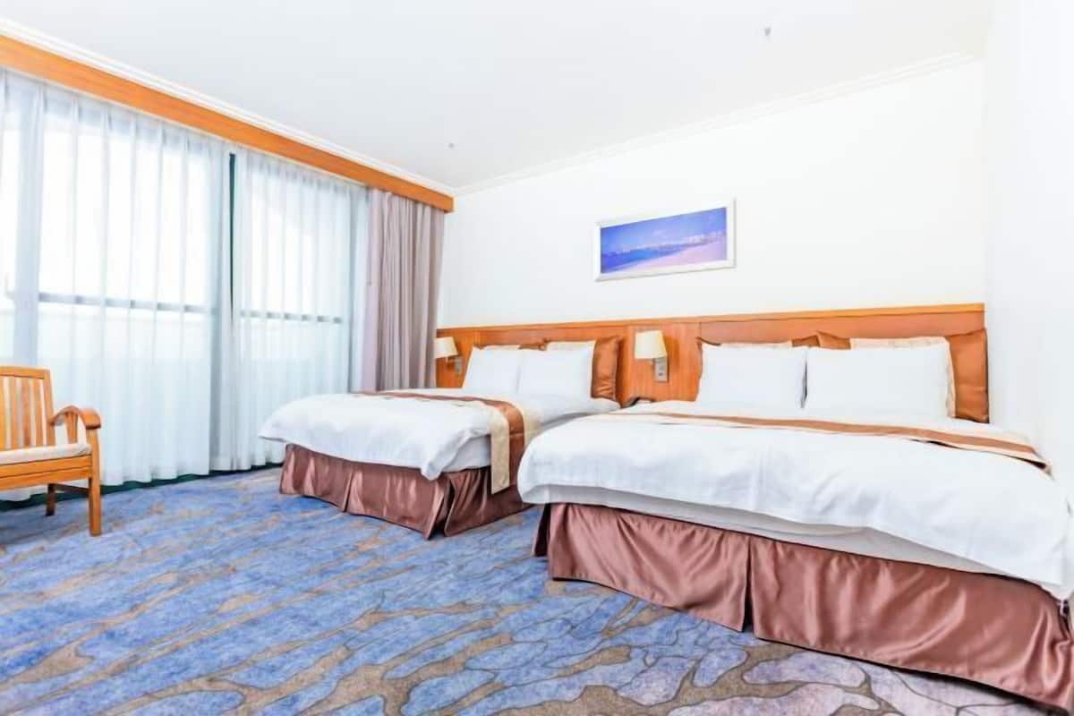 A hotel room with two beds, a wooden bench, a painting on the wall, and a patterned carpet.