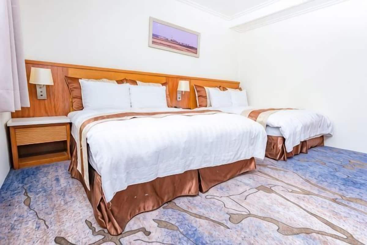 A hotel room with two beds, a wooden headboard, a nightstand, and a framed picture on the wall.
