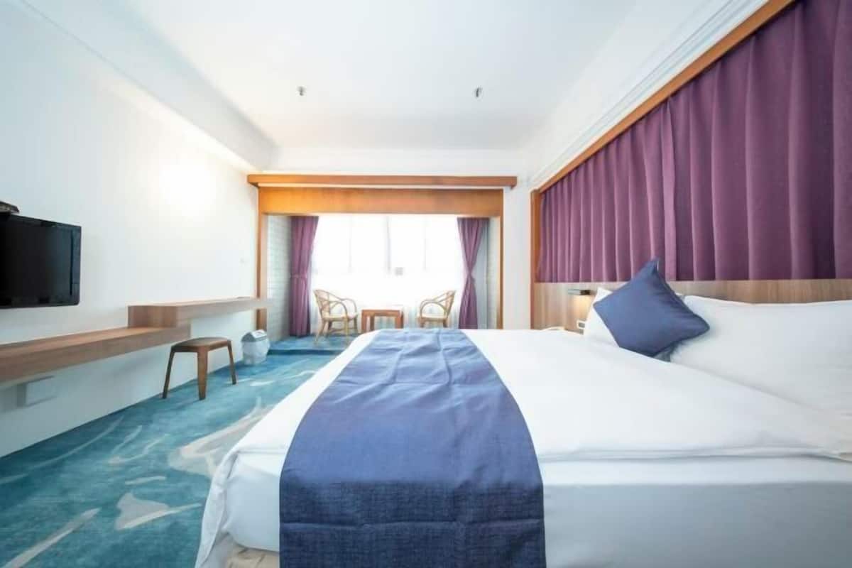 Habitación de hotel con cama, televisión de pantalla plana, escritorio, silla y ventana con cortinas.