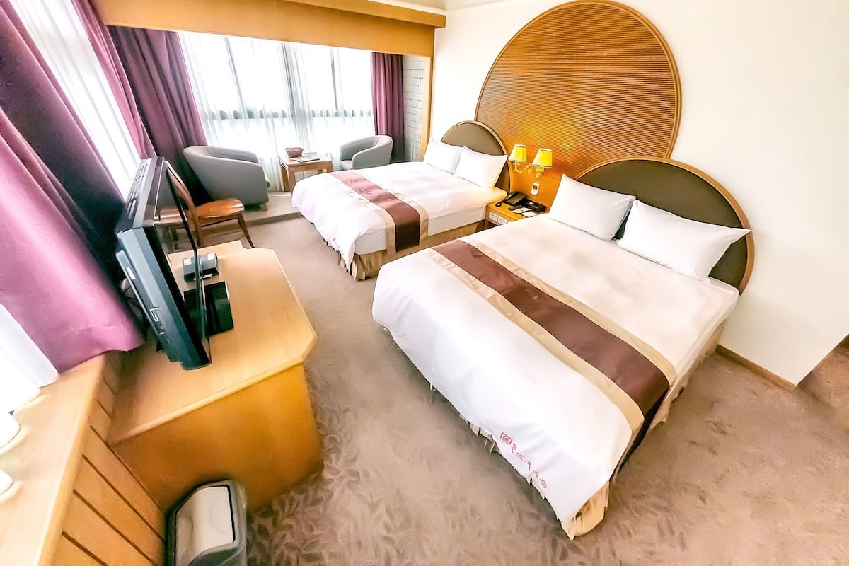 Habitación de hotel con dos camas, un escritorio, una silla, un televisor y una decoración circular grande en la pared.