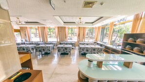 Un restaurant avec plusieurs tables, des chaises et un comptoir où sont empilées des assiettes.