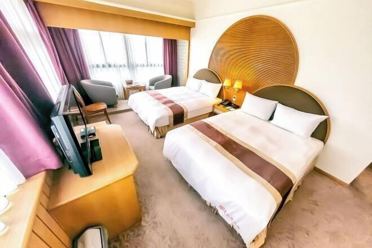 Habitación de hotel con dos camas, un escritorio con televisor, una silla y un adorno redondo en la pared.
