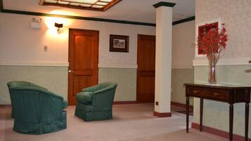 Una habitación con dos sillones verdes, una puerta de madera, un cuadro en la pared y un jarrón con flores rojas sobre una mesa.