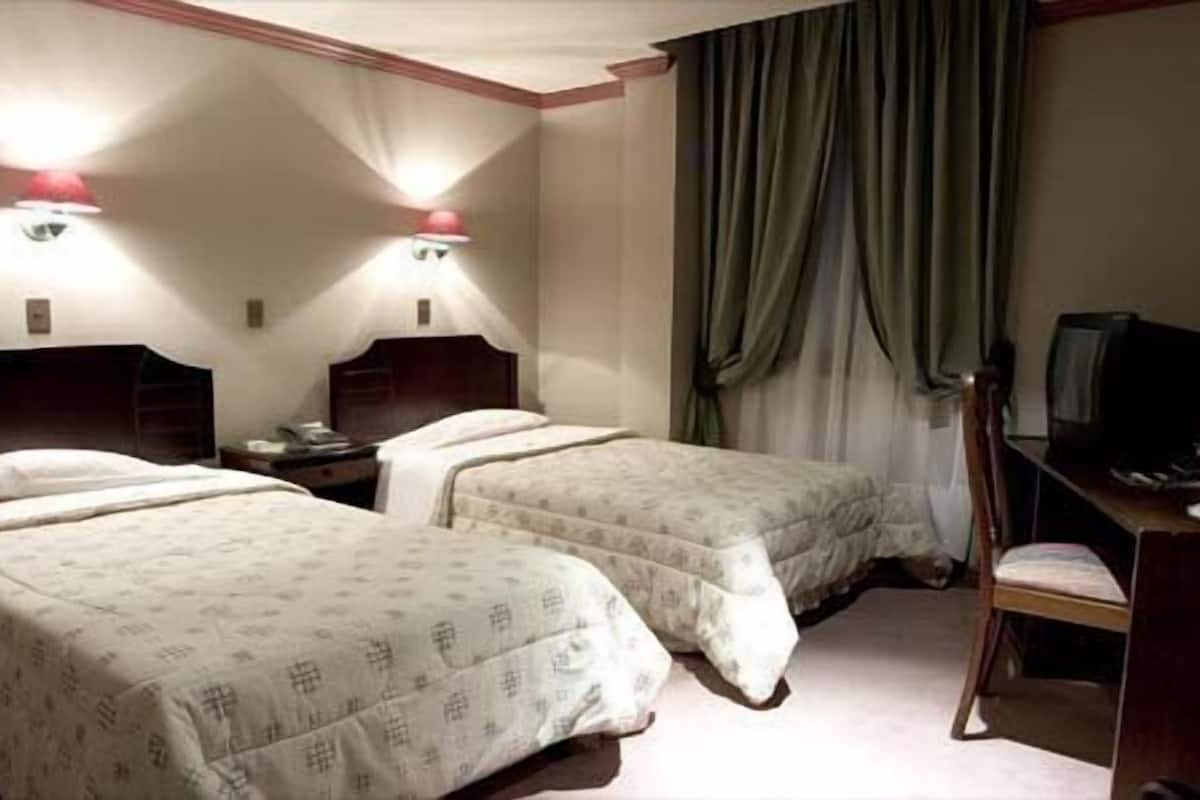 A hotel room with two beds, a desk, a chair, and a television.
