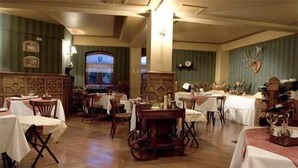 A dining area with tables set for meals, a vintage cart, and a decorative wall. - Hotel Isla Rey Jorge (Punta Arenas)