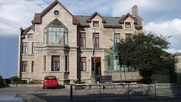 A large, historic building with a prominent clock tower, a large arched window, and a flagpole. - Hotel Isla Rey Jorge (Punta Arenas)