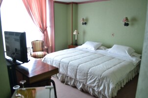 Una habitación de hotel con una cama, un escritorio con ordenador, una silla y una lámpara.