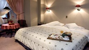 A hotel room with a large bed, a small round table with a red tablecloth, and two wall-mounted lamps. - Hotel Isla Rey Jorge (Punta Arenas)