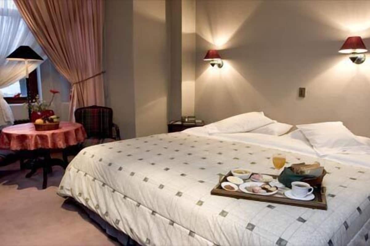 A hotel room with a large bed, a small round table with a red tablecloth, and two wall-mounted lamps.