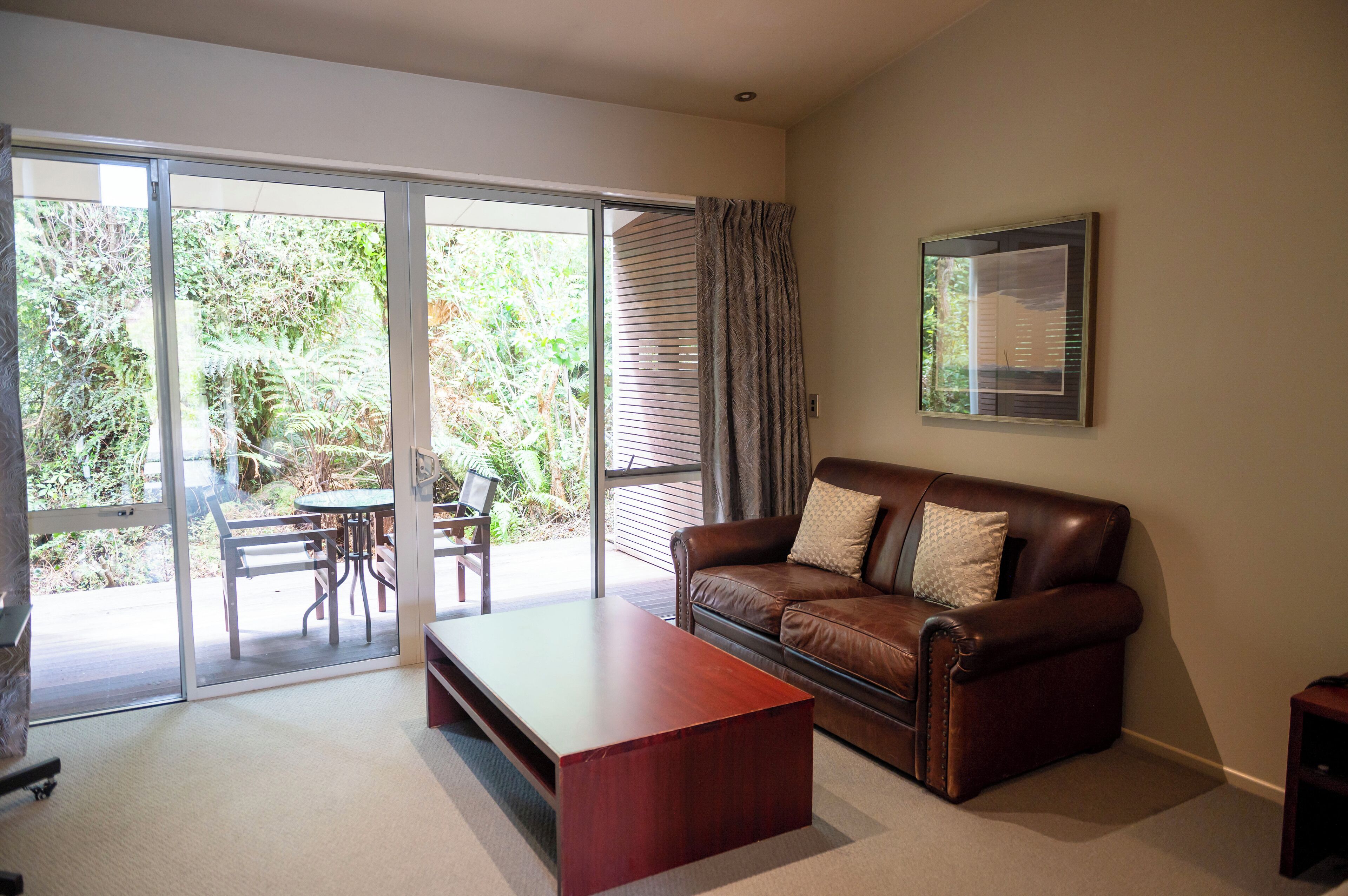 A living room with a brown leather sofa, a wooden coffee table, and a sliding glass door leading to a patio with a table and chairs.