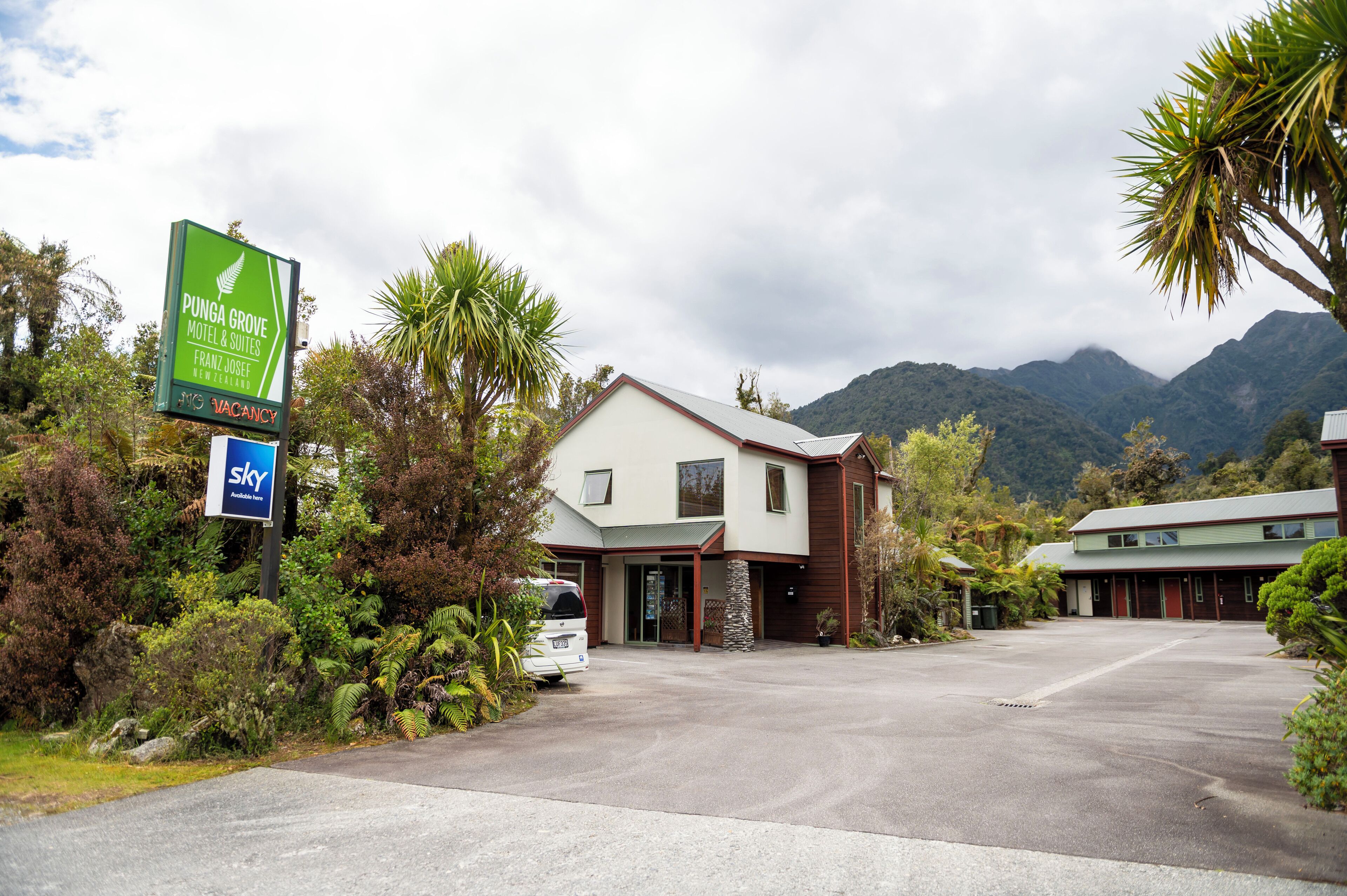 Un motel con un letrero que indica disponibilidad, rodeado de exuberante vegetación y montañas al fondo.