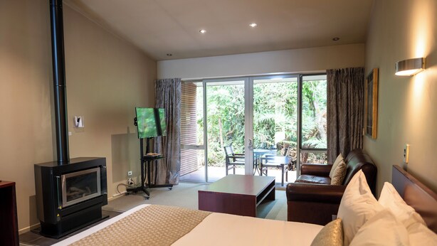 Une chambre d’hôtel comprenant un lit, un canapé, une petite table, une télévision, une cheminée et une porte-fenêtre coulissante donnant sur un patio aménagé avec du mobilier d’extérieur.