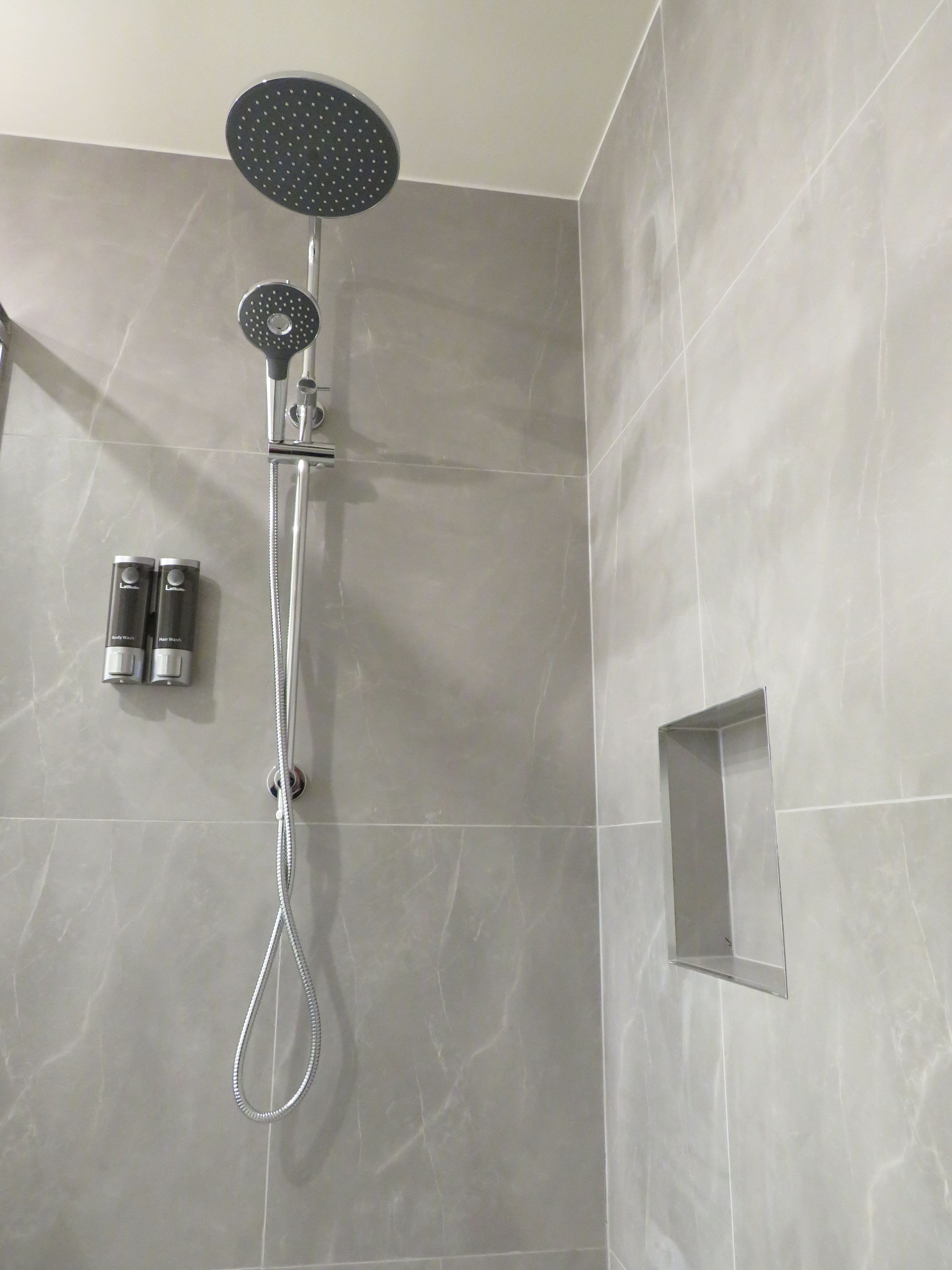 A modern shower with a rain shower head and handheld shower attachment, mounted on a wall with a marble finish.