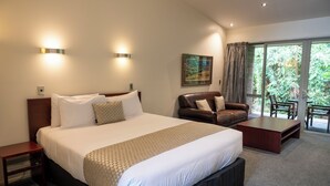Une chambre d’hôtel avec un grand lit, un canapé en cuir, une table basse et un balcon donnant sur un paysage verdoyant.