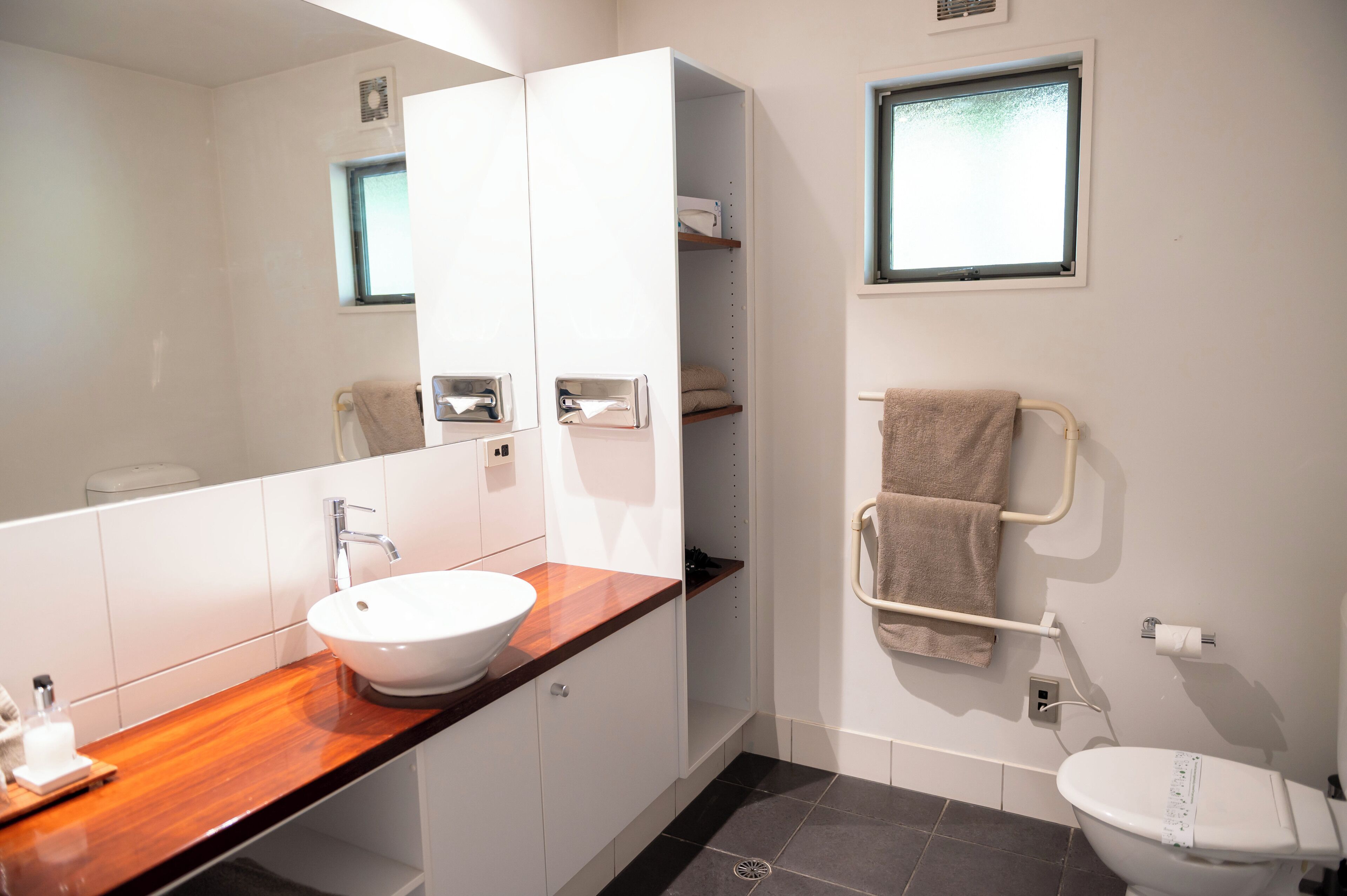 A modern bathroom with a wooden vanity, a white sink, a towel rack, and a toilet.