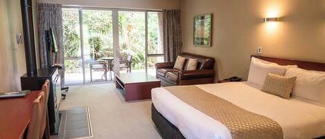 A hotel room with a large bed, a desk, a chair, a sofa, and a sliding glass door leading to an outdoor area.