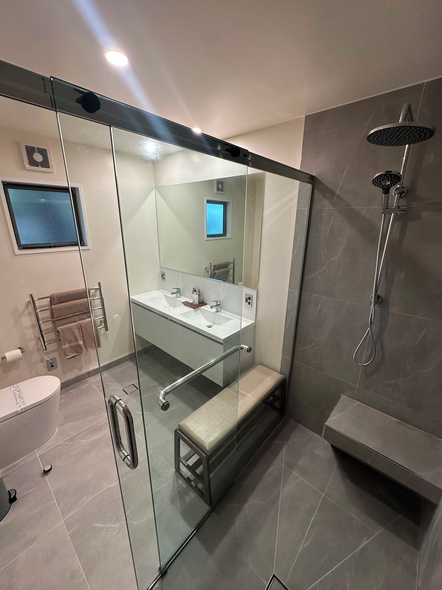 Un baño moderno con ducha envuelta en vidrio, tocador con espejo y retrete.