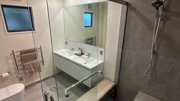 Un baño moderno con ducha envuelta en vidrio, tocador con espejo y retrete.