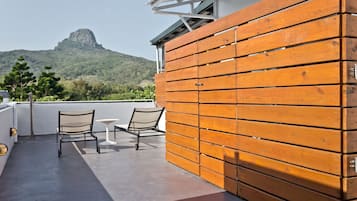 Terraza en la azotea con vistas a una montaña, paneles de madera, dos sillas y una mesita.
