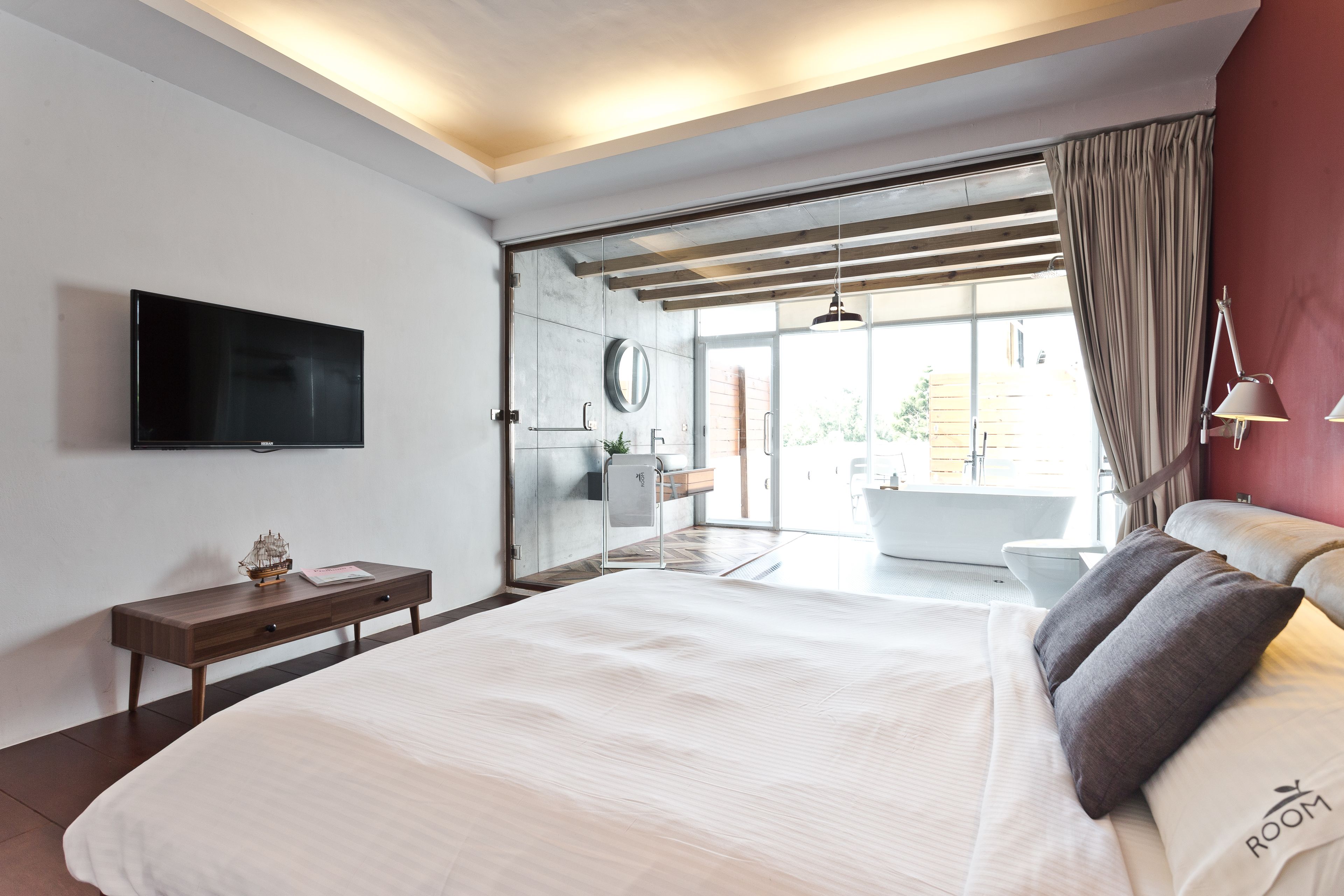 Un dormitorio moderno con una cama grande, un televisor de pantalla plana, una mesita de noche con un modelo de barco y vistas al baño y al exterior.